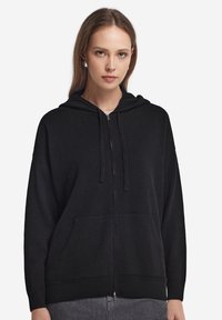Czarna bluza z kapturem na zamek, wykonana z miękkiego materiału, z przednią kieszenią, kapturem ze sznurkiem oraz ribbowanymi mankietami i dołem.