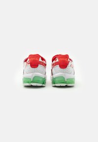 Vita idrottsskor i vitt med röda accenter och en genomskinlig grön sula. Funktioner inkluderar meshmaterial och "Coca-Cola"-logotyp på hälen.