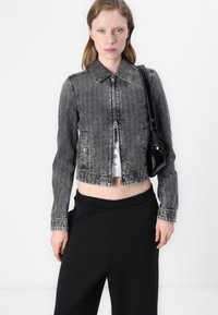 Γκρι κοντό τζάκετ από τζιν με γιακά, κεντρικό φερμουάρ και ελαφριά φθορά. Συνδυάζεται με μαύρες φαρδιές παντελόνες και μια μικρή μαύρη τσάντα.