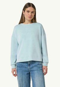 Lichtblauwe sweatshirt met een ronde hals, drop shoulders en reliëftekst "CASUAL". Gepaard met vervaagde blauwe jeans. Zachte, gladde textuur.