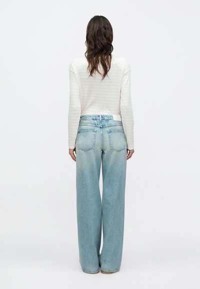 Jean large bleu clair avec une finition délavée, cinq poches et une ceinture classique. Associé à un haut à manches longues blanc rayé.