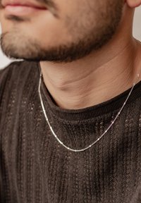 Collier en argent avec un design élégant, présentant des maillons plats et ronds alternés, reposant sur un pull en tricot texturé foncé.