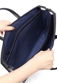 Sort håndtaske med en marineblå inderside, der har to rum og en lynlås-lomme. Ydersiden har en glat overflade og lynlås-lukning.