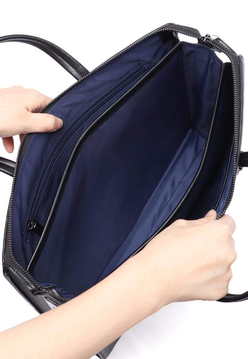 Sort håndtaske med en marineblå inderside, der har to rum og en lynlås-lomme. Ydersiden har en glat overflade og lynlås-lukning.
