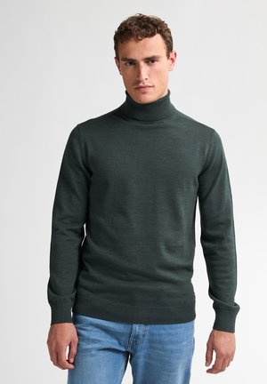 Dunkelgrüner Rollkragenpullover aus weichem Material, mit langen Ärmeln und geripptem Saum. Kombiniert mit hellblauen Denim-Jeans.