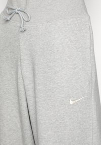 Lys grå bomull joggebukser med ribbet midje, snøring og en liten brodert Nike-logo i lys gull.