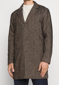 Brauner Herringbone-Mantel mit Reverskragen, drei Knöpfen und vorderen Taschen; strukturierter Stoff; taillierte Passform.