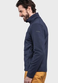 Navy-Fleecejacke mit Stehkragen, ausgestattet mit einem strukturierten Muster, einer Reißverschlusstasche und dezenten Branding am Ärmel.