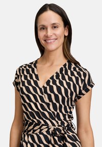 Abito a portafoglio in beige e nero, con motivo a onde, maniche corte, scollo a V e vita regolabile con laccio per una vestibilità personalizzabile. Tessuto dalla consistenza morbida.