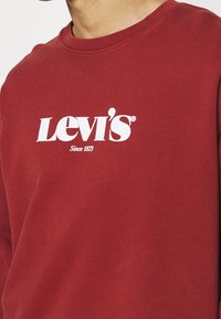 Felpa rossa in cotone, con logo Levi's bianco e scritta "Since 1873" sul petto. Design classico con collo rotondo, tessuto morbido.