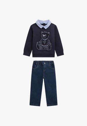Felpa blu navy con colletto azzurro e grafica di un orso, abbinata a pantaloni di jeans scuri con vita elastica e tasche standard.