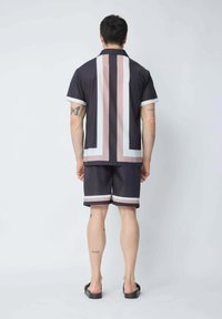 Ensemble chemise à manches courtes et shorts en bleu marine foncé avec des rayures verticales en rose clair et blanc. Tissu lisse ; col simple, idéal pour les activités de plein air.