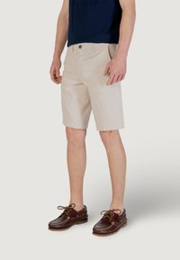 Shorts en coton beige avec une coupe droite et des poches avant, associés à des chaussures bateau en cuir marron avec des lacets. Design simple et décontracté.