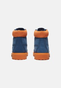 Botas de cuero azul con un cuello de ante naranja y suela de goma. Presentan un tobillo acolchado y detalles de costura para mayor textura.