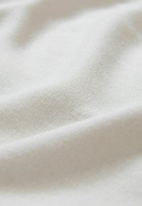 Tissu doux de couleur blanc cassé avec une texture tissée subtile et de douces plis créant de légères ombres sur la surface.