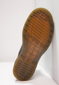Black rubber shoe sole with textured grooves, featuring a clear, raised logo and safety markings indicating oil and acid resistance.