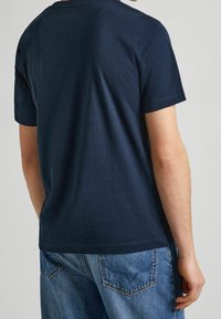 Camiseta de algodón azul marino con mangas cortas y cuello redondo, exhibida desde la parte de atrás. Combinada con jeans de mezclilla azul claro.