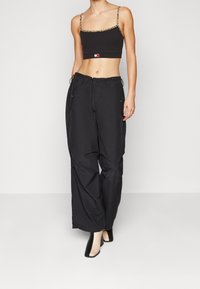 Top corto nero con spalline a stampa leopardo, abbinato a pantaloni neri morbidi. I pantaloni presentano una vita elasticizzata e tasche laterali.
