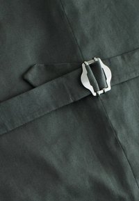 Dark green fabric with a smooth texture, featuring a shiny silver buckle and a reinforced strap detail for fastening.