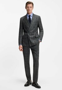 Grijze geruite dubbel-breasted pak met een getailleerde pasvorm, geknikte revers en zijzakken, gecombineerd met een lichtblauw shirt en zwarte schoenen.