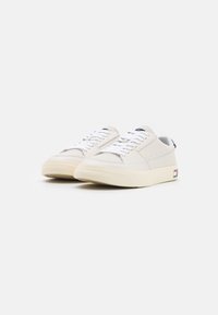 Zapatillas de piel blanca con una suela texturizada de color crema, que presentan cordones blancos, perforaciones en la parte superior y un peque�ño logo de color en el talón.