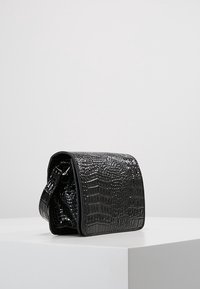 Borsa a tracolla nera in pelle sintetica con motivo coccodrillo, forma rettangolare, parte superiore arrotondata e tracolla removibile.