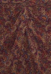 Flödande tyg med en mörkröd bakgrund, som har intrikata blomstermönster i guld, blått och orange, med en texturerad yta.