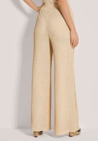 Beige wijde broek met gestructureerde gebreide stof, hoge tailleband en losse pasvorm. Geaccentueerd door een subtiel patroon en een ontspannen silhouet.