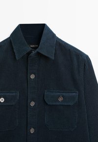 Camicetta in velluto a coste blu navy con colletto alla francese, chiusura a bottoni e due tasche con patta. Tessuto testurizzato con coste verticali e bottoni in contrasto.
