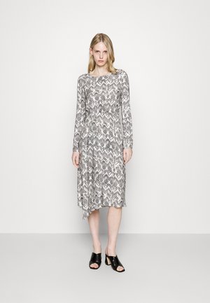 Langermet, grå kjole med abstrakt svart-hvitt mønster, midjebånd, asymmetrisk hem og glatt tekstur. Kombinert med svarte hælsandaler.