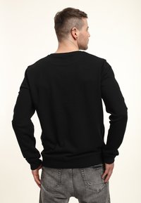 Sudadera negra de manga larga, con cuello redondo y puños acanalados. Textura suave, con un diseño sencillo sin patrones ni acentos.