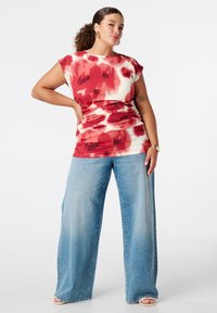 Rood en wit tie-dye top met korte mouwen, gecombineerd met wijde lichtblauwe jeans, waarbij een gestructureerde stof en een relaxte pasvorm worden getoond.