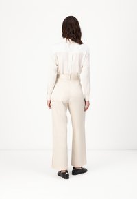 Pantalons larges de couleur crème avec une coupe ajustée et des fentes latérales, associés à un chemisier long à manches longues léger et transparent dans une teinte neutre.