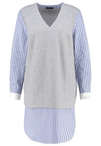 Top de mezcla de lana gris con escote en V, superpuesto sobre una camisa de algodón a rayas azul y blanca. Puños blancos acentúan las mangas de la camisa.