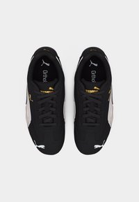 Ζεύγος μαύρων παπουτσιών Puma με λευκές λωρίδες στα πλάγια, χρυσά λογότυπα Puma και μαύρα κορδόνια, σε άποψη από πάνω σε λευκό φόντο.