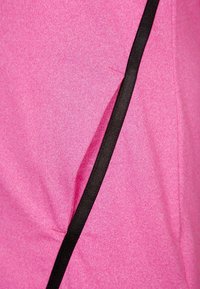 Růžová látka s jemnou texturou, s černým lemováním podél jednoho švu; konstrukce je jednoduchá s mírným nabráním na povrchu.