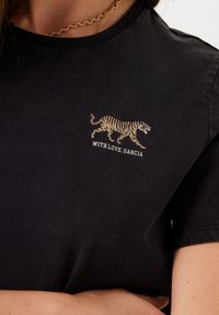 Camiseta negra de algodón con escote redondo, que presenta un gráfico de un tigre dorado y el texto "CON AMOR, GARCÍA" debajo.