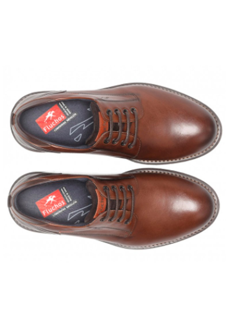 Zapatos de cuero marrón con punta redonda, diseño de cordones, costuras visibles y una plantilla texturizada que presenta el logo de Fluchos.