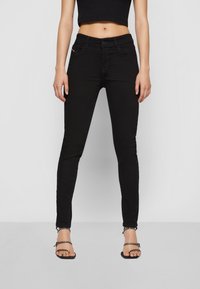 Jeans negros ajustados con una cintura de altura media, que presentan costuras sutiles, bolsillos frontales y una textura suave. Llevados con sandalias negras minimalistas.