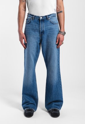Light blue flared jeans made of denim, featuring a high waist, five pockets, and subtle fading. Paired with black shoes.