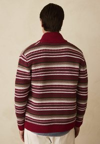 Knitted sweater with a fold-down collar, featuring red, white, and green stripes in a geometric pattern. Ribbed cuffs and hem.