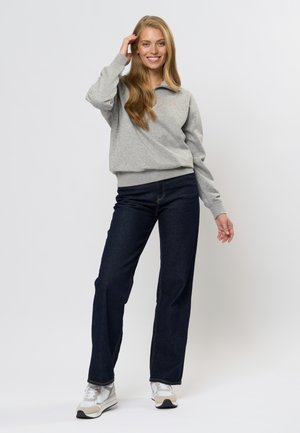 Grå fleecegenser med halv-zip krage, kombinert med mørkeblå denimjeans og hvite joggesko med grå detaljer.