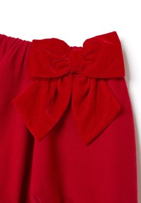 Tela roja con un gran lazo de terciopelo adjunto, mostrando textura y pliegues contra un fondo blanco liso.