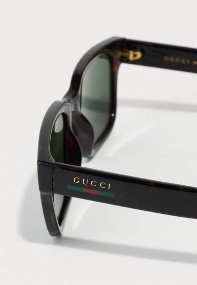 Kilpkonnamustriga päikeseprillid tumeroheliste läätsedega. Omab kuldset riistvara ja "GUCCI" logo külgedel, millele on lisatud rohelised ja punased ribad.