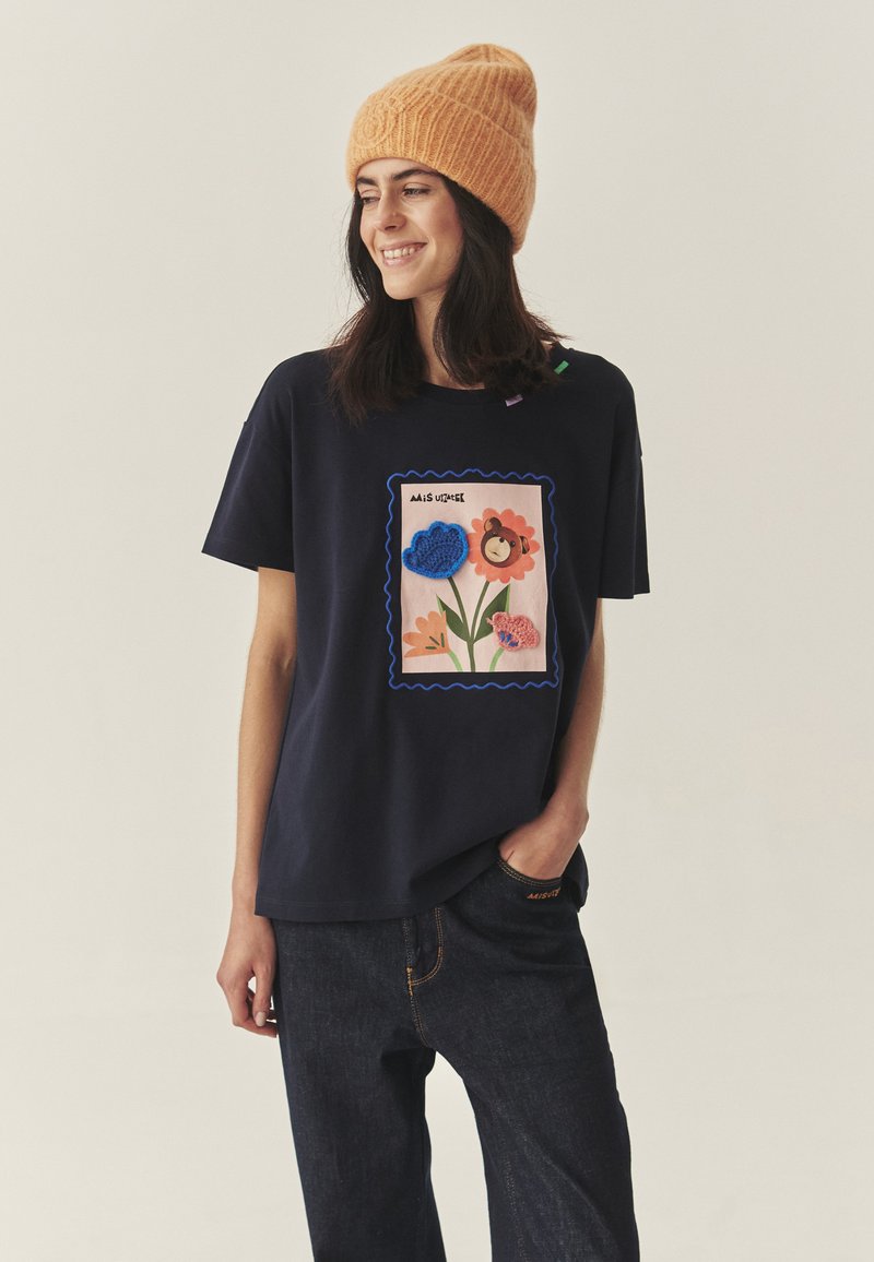 Tumesinine T-särk, millel on värvikas, tekstuuriga lille- ja looma kujutis. Omadusteks on ümara kaelusega ja mugava lõikega ning sobitatud tumedate teksapükstega.