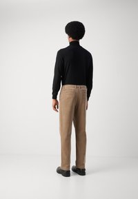Pantalones de pana marrones con un corte recto, bolsillos traseros y zapatos negros; combinados con una camiseta de manga larga negra ajustada.
