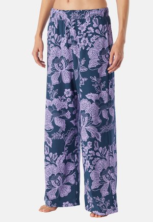 Weit geschnittene marineblaue Hose mit großem helllila Blumenmuster, getragen von einer Person, die barfuß steht und die Hände entspannt an den Seiten hält.