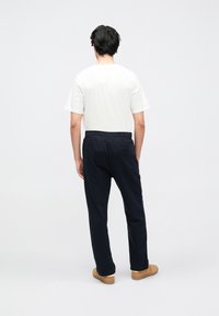 Sötét tengerészkék színű szabadidőnadrág elasztikus derékpánttal és oldalzsebbel, fehér pólóval párosítva, hátulról egy személyen viselve.