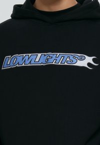 Zwarte hoodie met een grafische print aan de voorkant. Het logo "LOWLIGHTS" toont blauwe en witte tekst met vlamaccenten, op een gestructureerde stof.