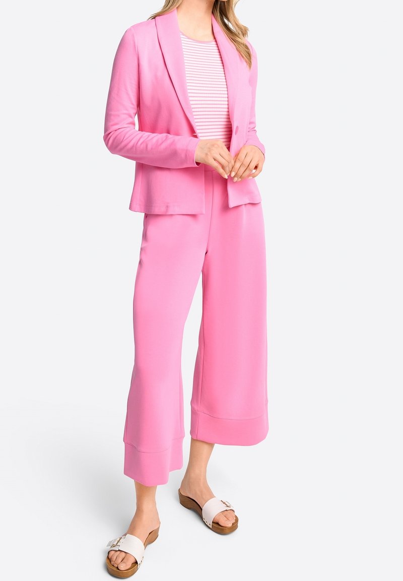 Blazer rosa e pantaloni a gamba larga realizzati in tessuto morbido, con una vestibilità comoda e rever a punta. Abbinati a sandali di colore chiaro.